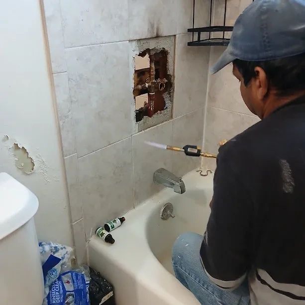Plumber repairing a shower valve behind bathroom tile